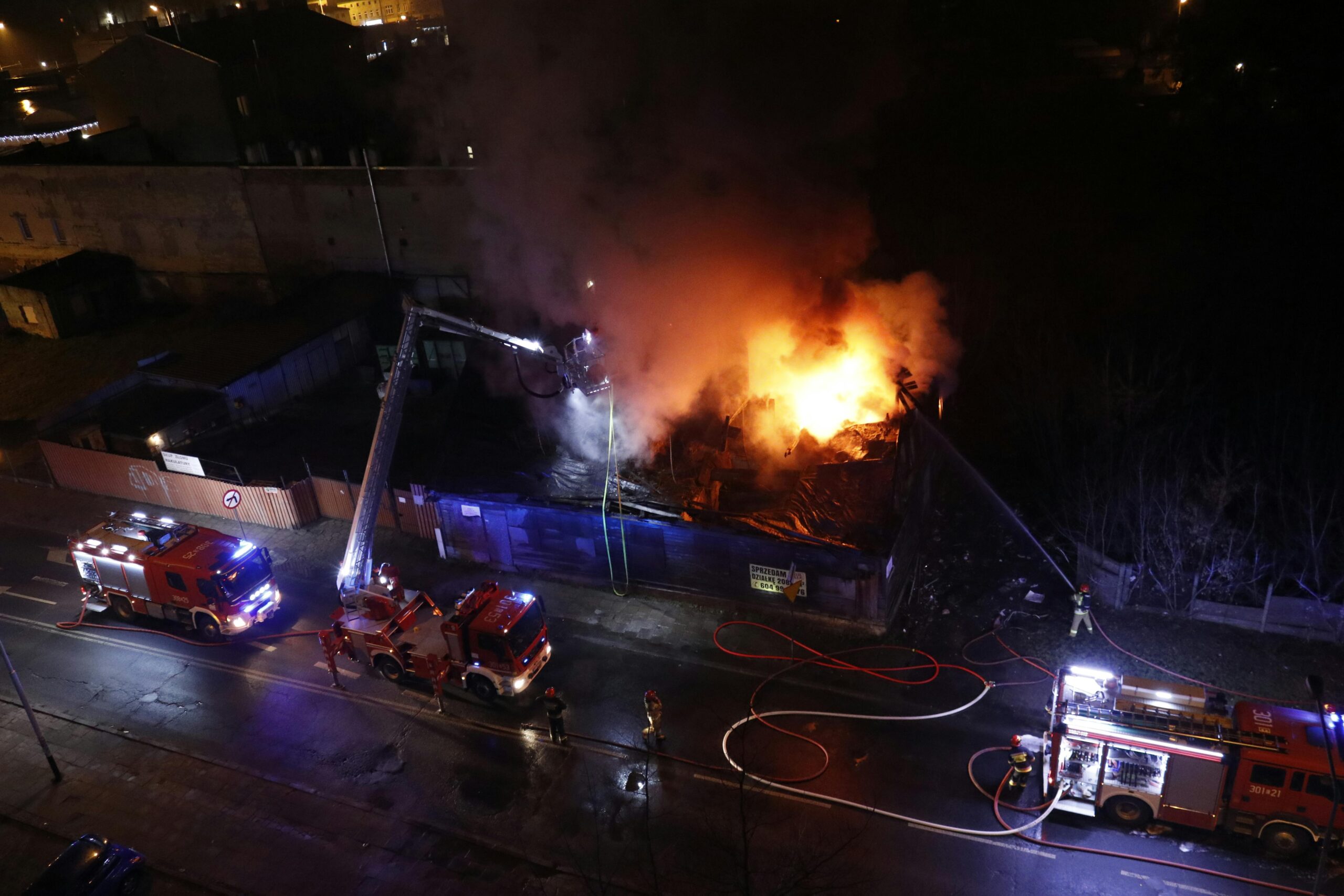 Firefighters battling a large blaze in a city at night, captured from above. Aerial view of emergency response.